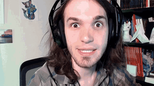 a man with long hair wearing headphones and a plaid shirt is smiling
