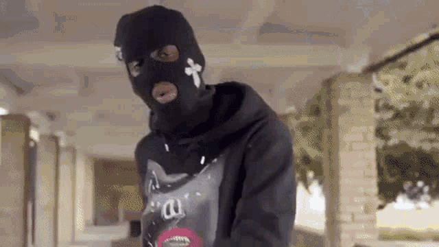a man wearing a ski mask and a hoodie is standing in a building .