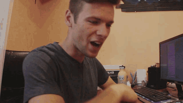 a man sitting in front of a computer with a bottle of iced tea