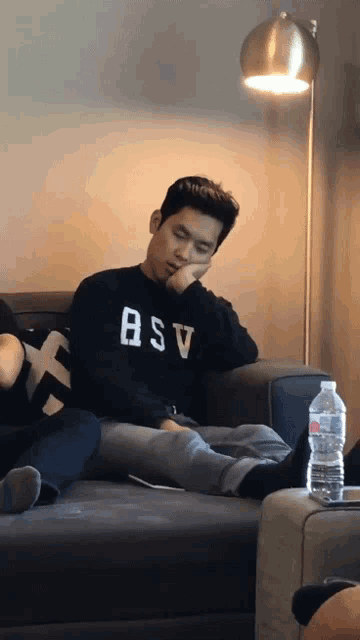 a man sitting on a couch wearing a black bsv sweatshirt