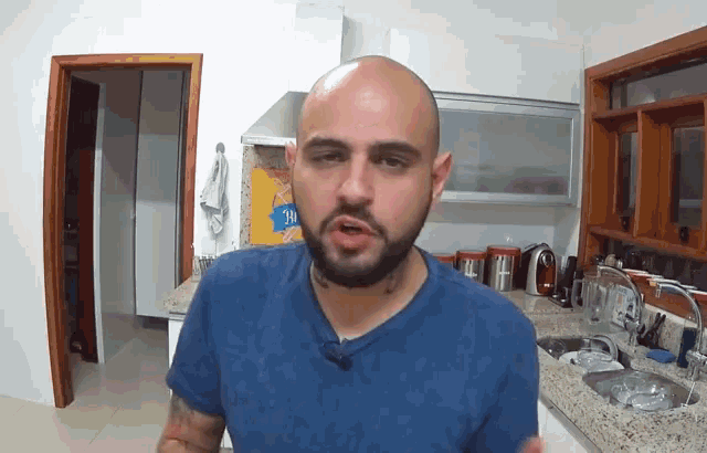 a bald man with a beard is standing in a kitchen with a bag of nestle chips behind him