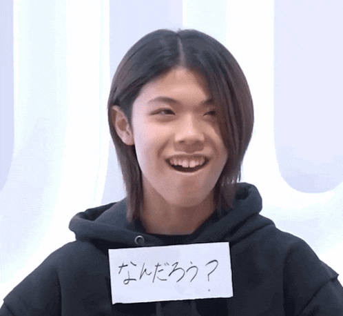 a young man wearing a black hoodie holds a piece of paper that says ' ? '