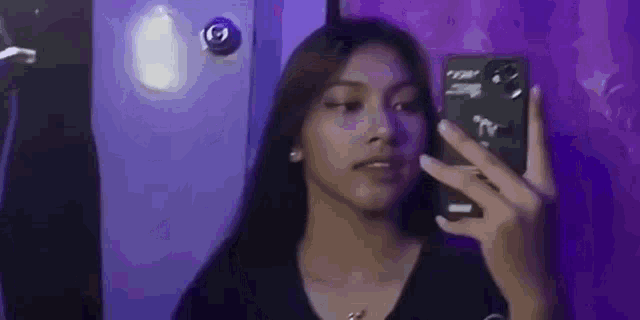 a woman is taking a selfie in front of a mirror with her phone .