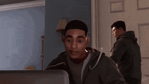 a man in a hoodie is looking at a computer screen in a room .