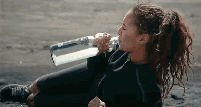a woman is sitting on the ground drinking from a glass bottle .