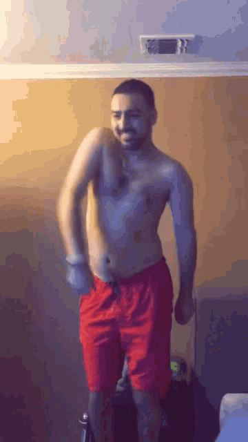 a shirtless man in red shorts is dancing with a suitcase in the background