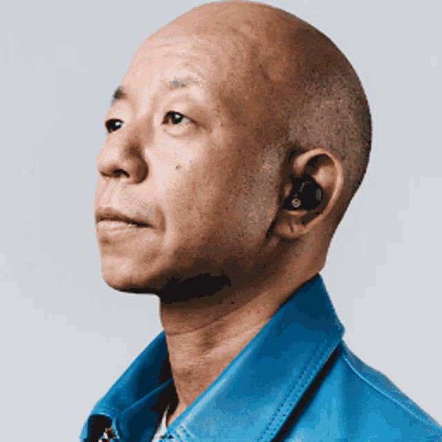 a bald man wearing a blue leather jacket and black ear buds