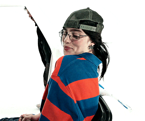 a woman wearing glasses and a hat is smiling and looking over her shoulder