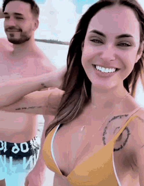 a woman in a yellow bikini smiles while a man in black shorts with the number 60 on them smiles behind her