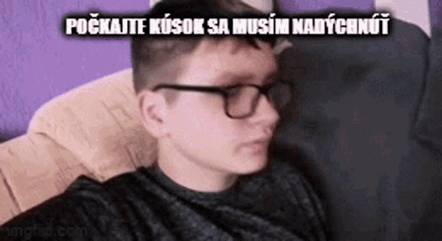 a young boy wearing glasses is sitting on a couch and taking a selfie .