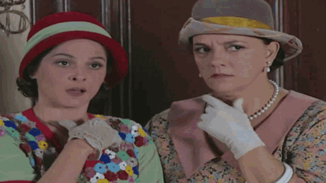 two women wearing hats and white gloves are looking at each other