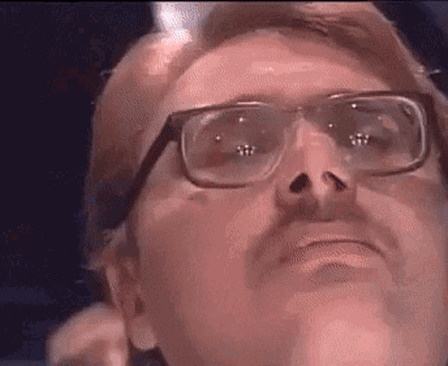 a man wearing glasses and a mustache is looking up at something .