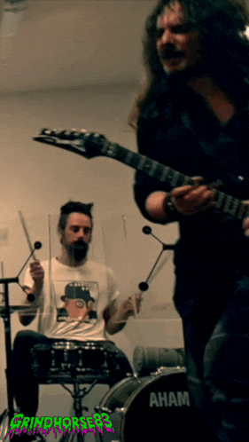 a man playing drums and a man playing a guitar with a drum set that says ' aham ' on it