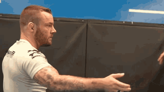 a man with a tattoo on his arm is wearing a white shirt that says mma on the back