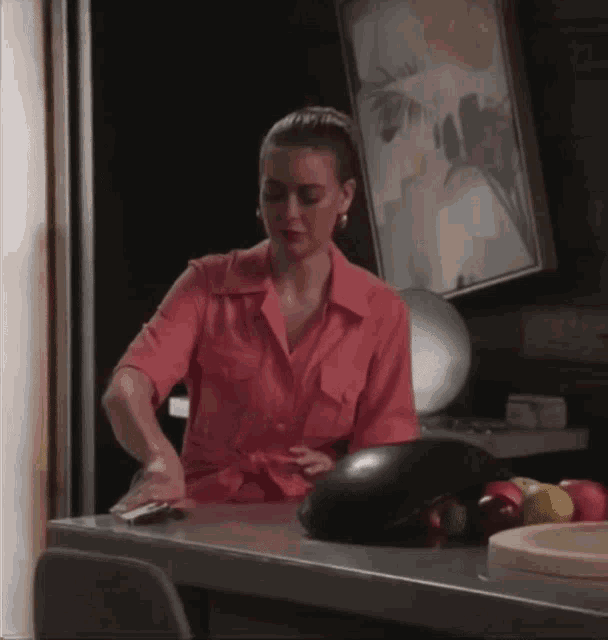 a woman in a pink shirt sits at a counter with a large eggplant on it