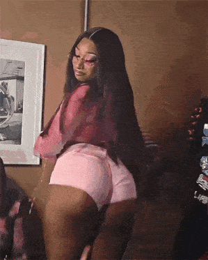 a woman wearing pink shorts and glasses is dancing in front of a framed picture