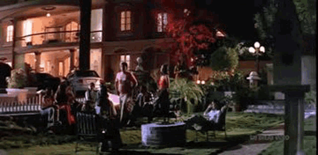 a group of people are sitting around a fire pit in front of a large house at night .