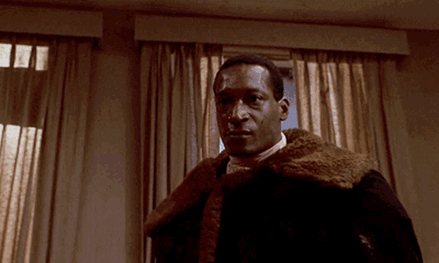 a man in a fur coat stands in front of a window with curtains