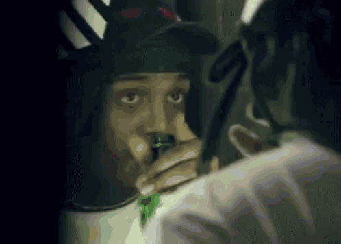 a man is smoking a cigarette in front of a mirror while wearing a hat and a bandana .