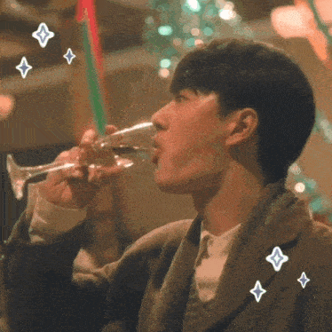 a man is drinking from a glass with a christmas tree in the background