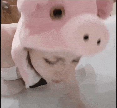 a woman wearing a pink pig hat and a bow tie is laying in a bathtub .