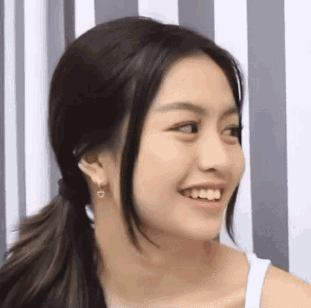 a close up of a woman 's face wearing a white tank top and earrings .