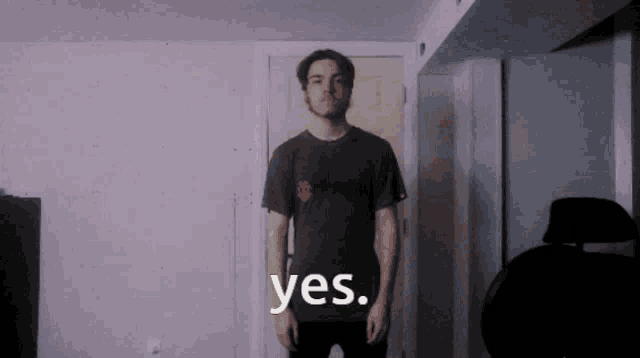 a man in a black shirt says yes in front of a white wall