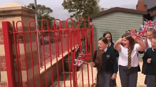 a group of children are walking through a red fence holding flags