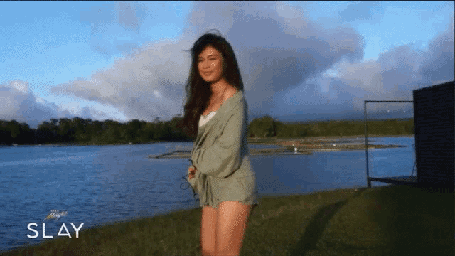 a woman is standing in front of a body of water and the word slay is above her