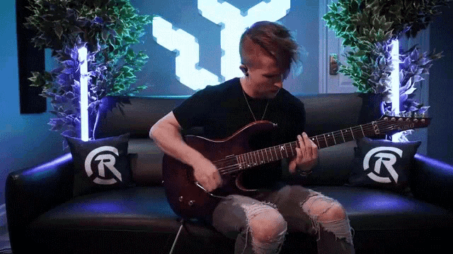 a man playing a guitar on a couch with pillows that say r