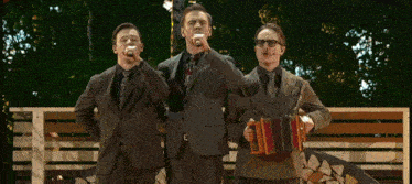 three men in suits and ties are singing and playing accordions