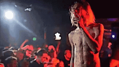 a man without a shirt is singing into a microphone in front of a crowd of people .