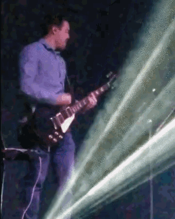 a man in a blue shirt is playing an electric guitar on stage