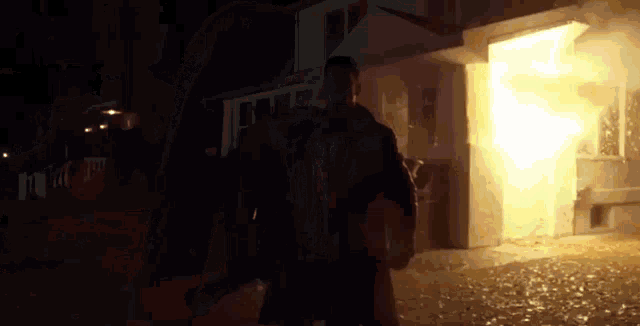 a man is standing in front of a house that is on fire at night .