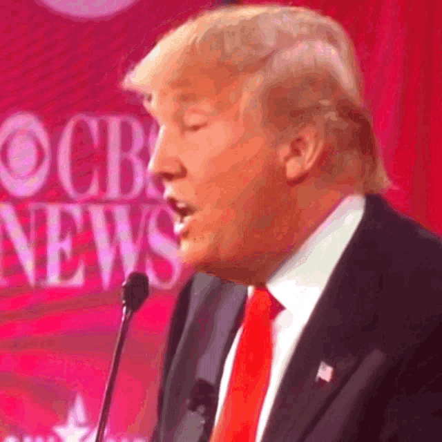 donald trump is speaking into a microphone in front of a cbs news sign