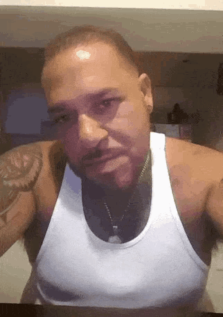 a man is wearing a white tank top and has a tattoo on his arm