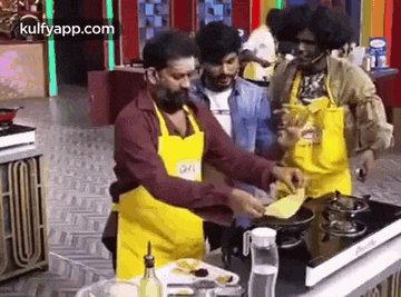 a group of men are standing around a table in a kitchen cooking food .