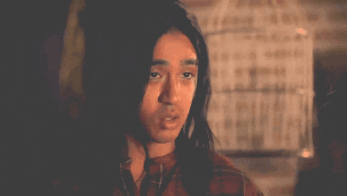 a man with long hair looks at the camera with a serious look on his face .