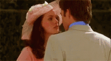 a woman in a pink hat is kissing a man in a white suit