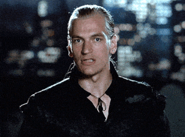 a man with a ponytail is wearing a black shirt and has a necklace around his neck