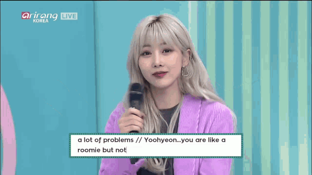 a woman in a purple jacket is holding a microphone in front of a sign that says arirang live korea