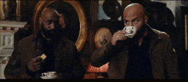 two bald men are sitting next to each other holding cups of tea