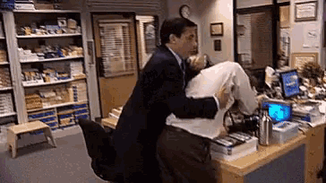 a man in a suit and tie is hugging another man in an office .