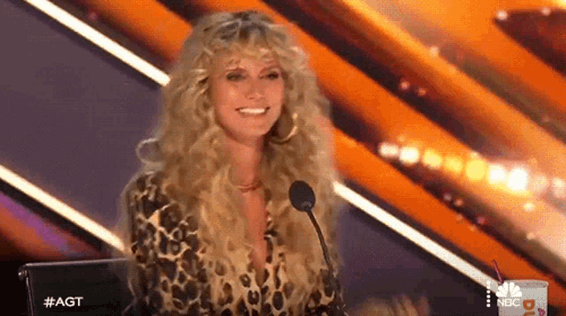 a woman in a leopard print shirt is sitting in front of a microphone and smiling .