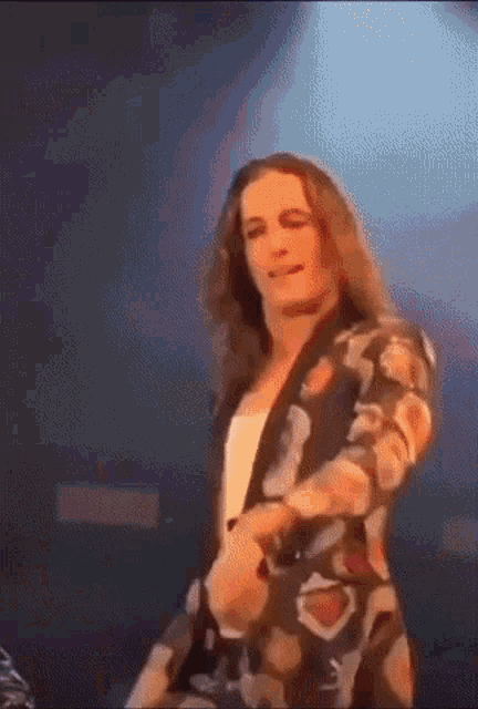 a man with long hair is dancing on a stage in a floral jacket .