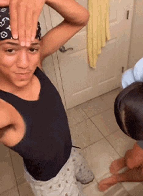 a man wearing a black tank top and a louis vuitton bandana holds his hands on his forehead