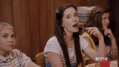 a woman is sitting at a table eating food with a fork and spoon .