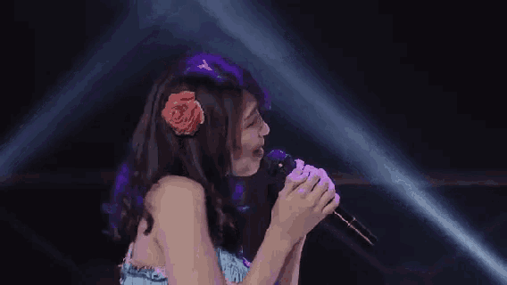 a woman is singing into a microphone on a stage with a flower in her hair .