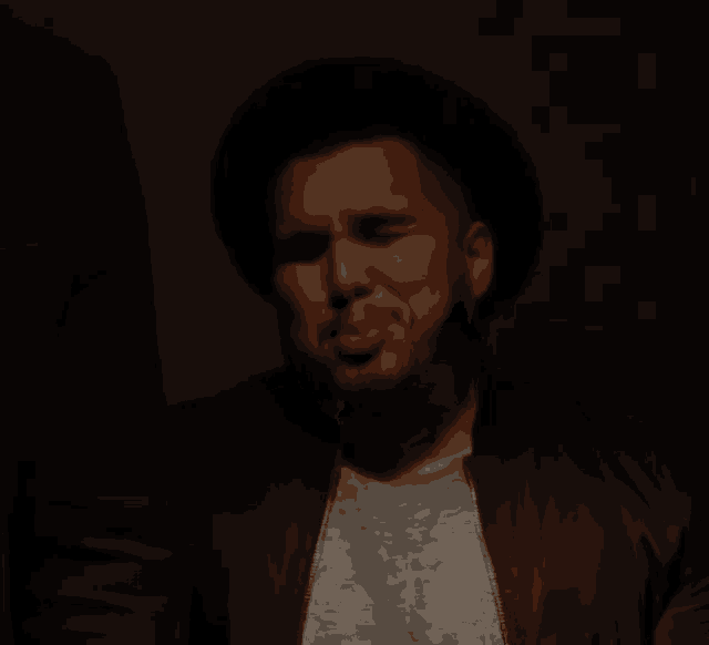 a man with a beard wearing a hat and a jacket making a funny face