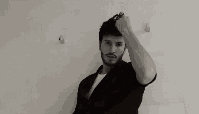 a man with a beard is standing in front of a white wall holding his hair .
